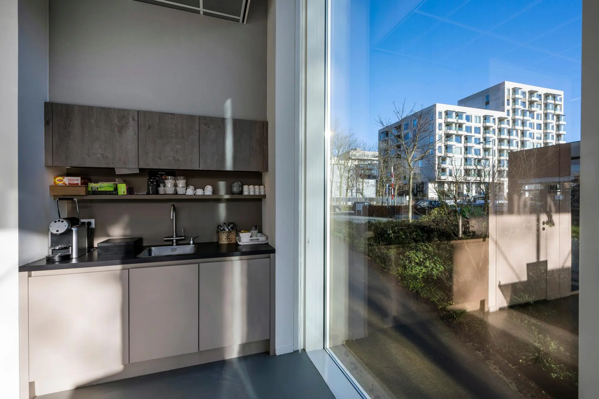 Kleine moderne pantry met koffieapparaat en spoelbak, met uitzicht op appartementencomplex aan de Fred. Roeskestraat.